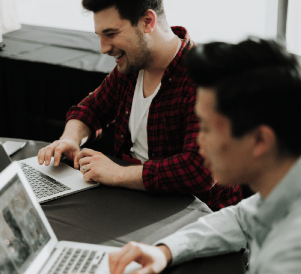 Two men, each looking at a laptop screen, one smiling